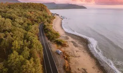 campervan beside the ocean in Cairns with the daintree rainforest behind it