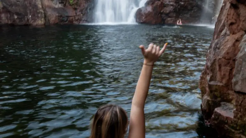 Woman in a bikini raising her arm by a stunning waterfall during the 4-Day Kakadu, Katherine, and Litchfield Adventure tour.