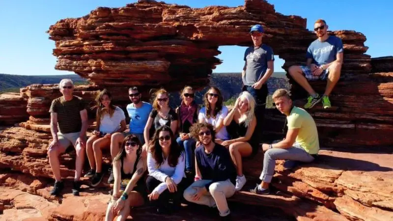 Travellers pose together on vibrant red rocks beneath a clear blue sky on a Broome to Perth West Coast Adventure tour, Australia.