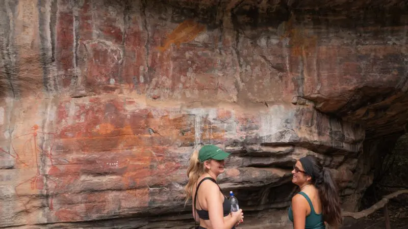 Two women explore ancient Aboriginal rock art during a 3 Day Kakadu Adventure Camping tour, available June–September in Australia.