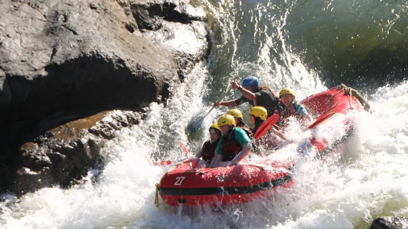 Thrill-seekers wearing helmets navigate challenging Barron River rapids in a red raft on a Half Day White Water Rafting Cairns tour.