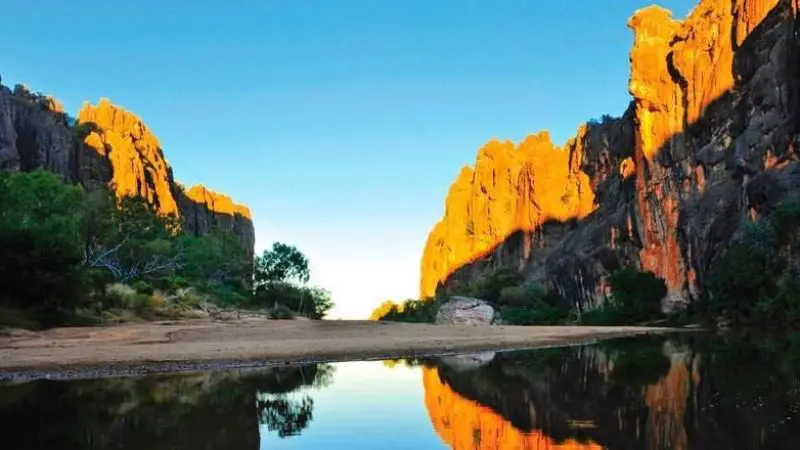 Stunning orange cliffs and lush green trees reflect in a tranquil river at sunset on a 10 Day Darwin to Broome 4WD Adventure tour.