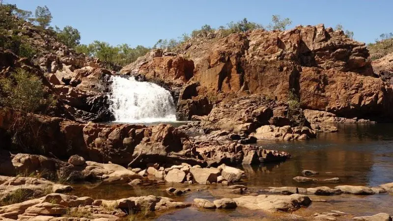 Stunning waterfall cascades into a rocky pool beneath clear blue skies, a must-see on the 10 Day Darwin to Broome 4WD Adventure.