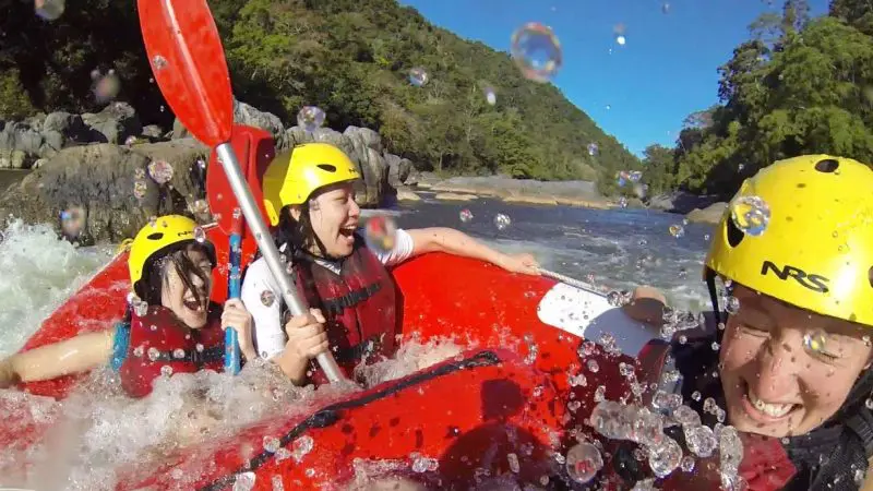 Smiling rafters in helmets and life jackets enjoy thrilling white-water rapids on a Half-Day Barron River Rafting tour near Cairns.