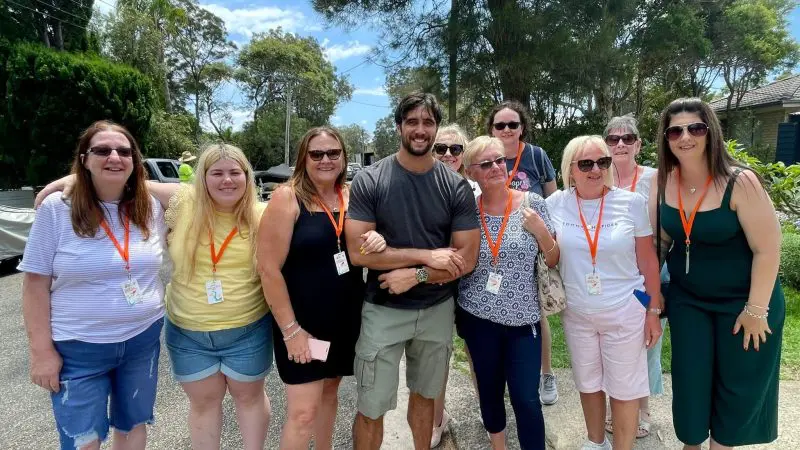 Ten adults wearing sunglasses and name tags smile on a sunny street during Celebtime Tours’ 1 Day Home Away Tour experience.