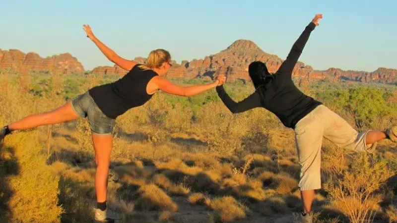 Two people balance on one leg, holding hands amid rocky hills on the 10 Day Broome to Darwin Kimberley 4WD Adventure Tour.