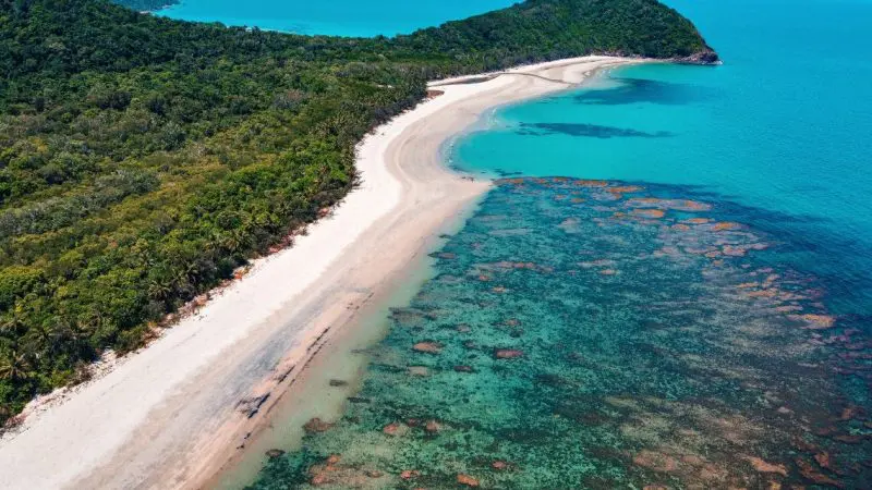 Stunning aerial view of Cape Tribulation: pristine white sand beaches, crystal-clear turquoise waters, and dense rainforest hills on a 1-day tour.