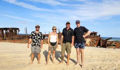backpackers exploring K'gari at Maheno shipwreck in the background with Peterpans