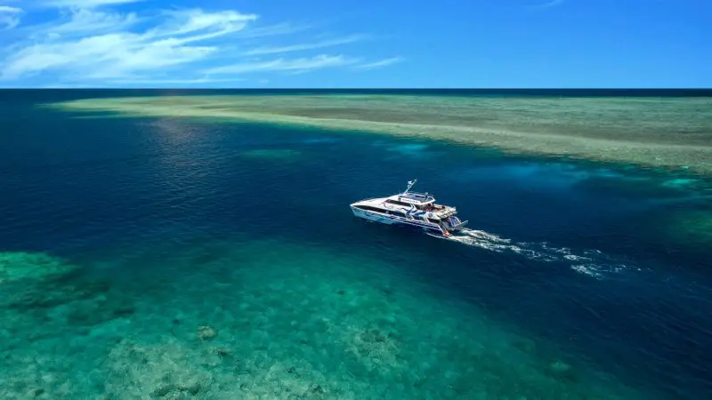 A dive boat glides over crystal-clear blue water as divers start their 2 Day 1 Night PADI Advanced Open Water Course by a thriving coral reef.