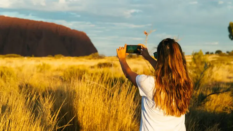 Traveller with flowing hair captures stunning sunlit Uluru during a 3-Day Uluru Rock The Centre Tour, departing Alice Springs.