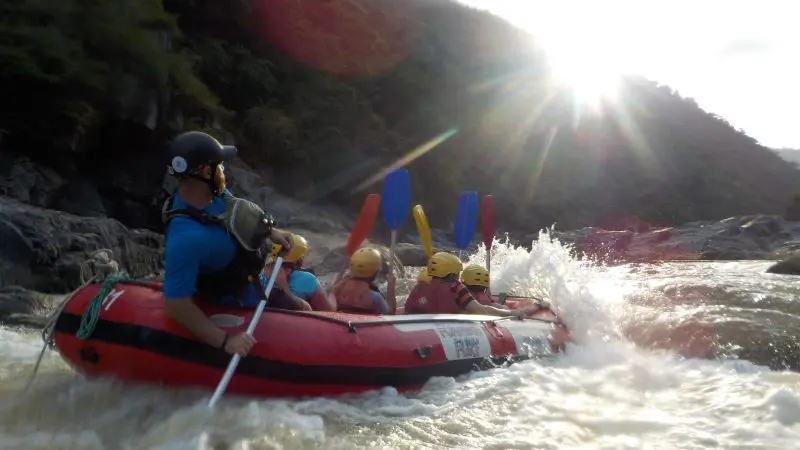 Adventurers white-water rafting Barron River near Cairns on a half-day tour, paddling rapids with sunlit hills in the background.