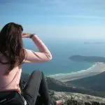 Woman on a Wilsons Promontory day tour with Go West Tours sits atop a rock, overlooking pristine beaches and vibrant blue sea views.