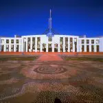 Parliament House Canberra, iconic landmark for day trips from Sydney, under clear blue skies and a striking patterned stone courtyard.