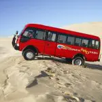Experience the thrill as a red 1 Day Port Stephens 4WD tour coach ascends sandy dunes with Colourful Collective Travel adventure tours.