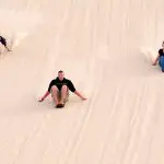 Three adventurers sandboard side by side down Port Stephens dunes with Colourful Collective Travel, experiencing an epic racing adventure.