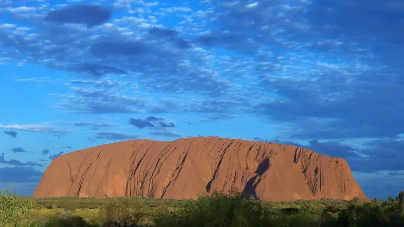 Uluru majestically towers under a vivid blue sky with scattered clouds on the 3 Night Uluru Rock The Centre Alice Springs to Yulara tour.