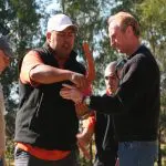 Group of four men on an Uncharted Blue Mountains Tour, enjoying a sunny day outdoors as one expertly demonstrates boomerang throwing skills.