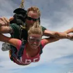 Two people tandem skydiving over Sydney, smiling and giving thumbs up above the clouds—experience top-rated Skydive Extras.