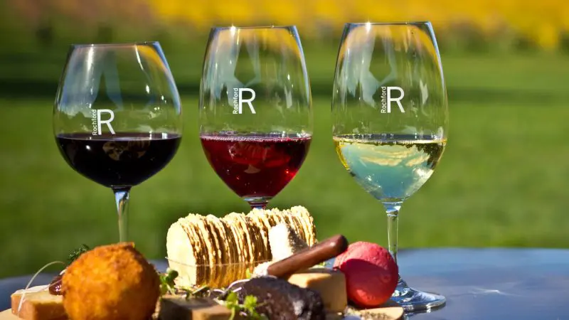 Elegant trio of Yarra Valley wines paired with gourmet appetisers and artisan crackers on a rustic board, ideal for outdoor grazing tours.