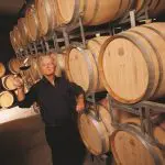 Yarra Valley Grazing Tour: man in atmospheric wine cellar showcasing premium red wine beside oak casks, highlighting local winery experience.