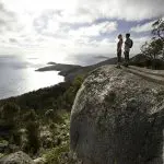 Two travellers on a rocky outcrop admire stunning Wilsons Promontory coastline during a top-rated 1 Day Go West Tours adventure.