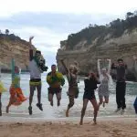 Group of eight people leaps with excitement on a scenic beach during a 1 Day Great Ocean Road 12 Apostles Tour by Go West Tours.