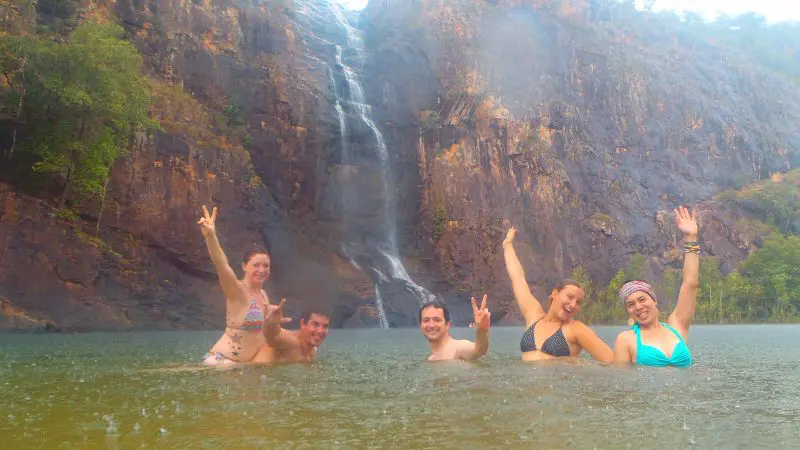 Group of five in swimsuits enjoying a natural pool beneath dramatic cliffs and waterfall on a 3 Day Kakadu Litchfield 4WD tour.