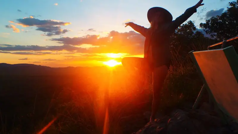 Adventurer in wide-brimmed hat does yoga tree pose atop scenic hill at sunset on 3 Day Kakadu Camping tour, June-September.