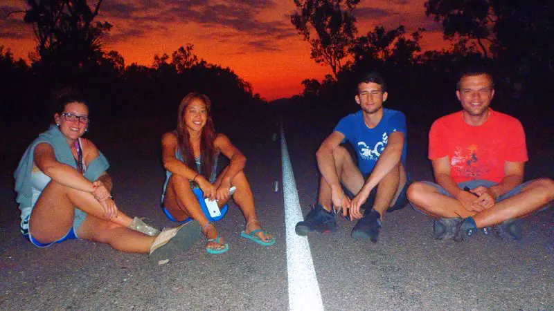 Four friends enjoy a sunset on an open road, smiling under vibrant skies—showcasing unforgettable Kakadu Tour Highlights.