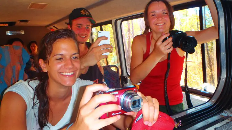 Three happy travellers on a 3-Day Kakadu 4WD Adventure Tour lean out of their vehicle, capturing sunlit photos in Australia’s outback.