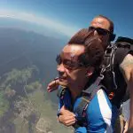 Experience an exhilarating Skydive Sydney tandem jump, soaring above lush green fields and forests under a stunning clear blue sky.