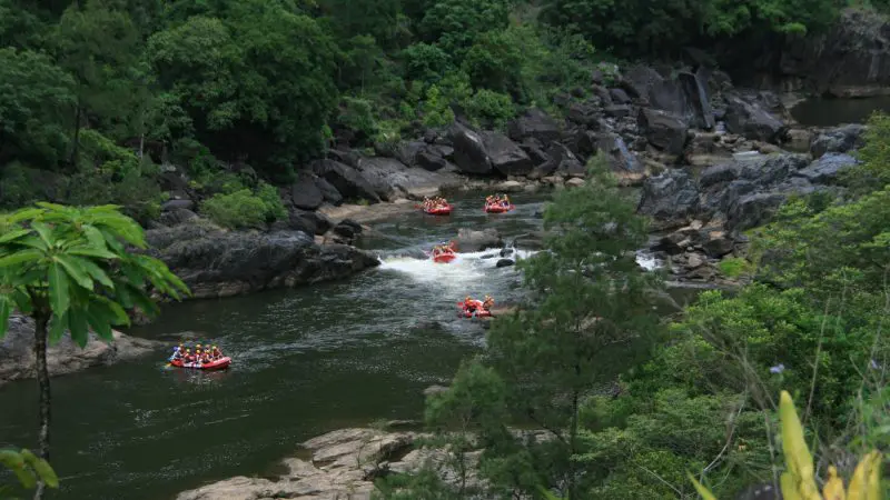Adventurers navigate thrilling white-water rafting on the Barron River near Cairns, amidst lush rainforest and dramatic rocky landscapes.