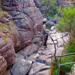 Scenic Grampians Day Tour: narrow rocky trail with railings winding through dramatic gorge, flanked by towering steep rock walls.