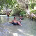 Experience two adventurers relaxing on rubber rings in a crystal-clear stream, surrounded by lush nature on a Kgari 2 Day Tour from Hervey Bay.