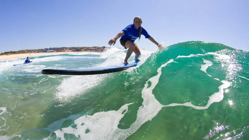 Surfer riding a vibrant green wave at Byron Bay in a 2-hour small group surf lesson under a clear blue sky, Australia’s top surf spot.