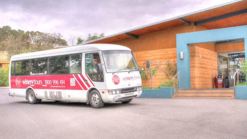 Yarra Valley Wine Experience coach outside a contemporary wooden winery, inviting visitors under overcast skies for premium wine tours.