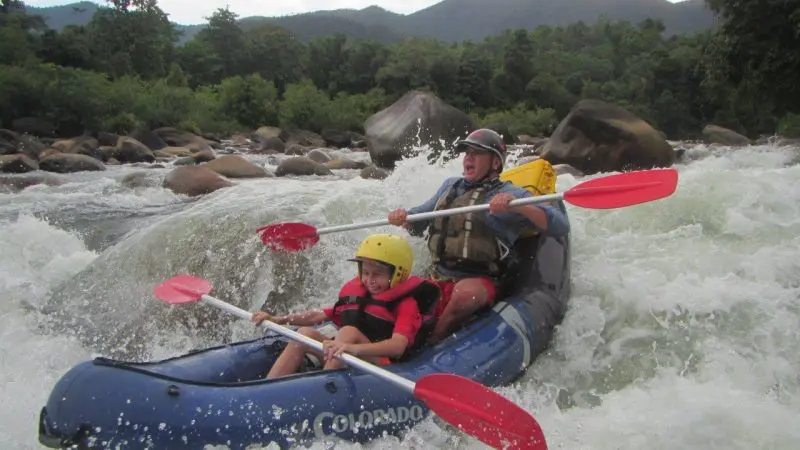Adventurers wearing helmets paddle a blue raft through thrilling white-water rapids on a full-day Mission Beach rafting experience.