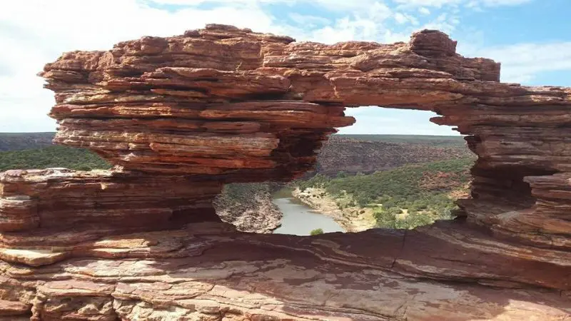 Stunning red rock arch with natural window on the 8 Day Perth to Exmouth Tour, overlooking scenic river and lush green countryside.