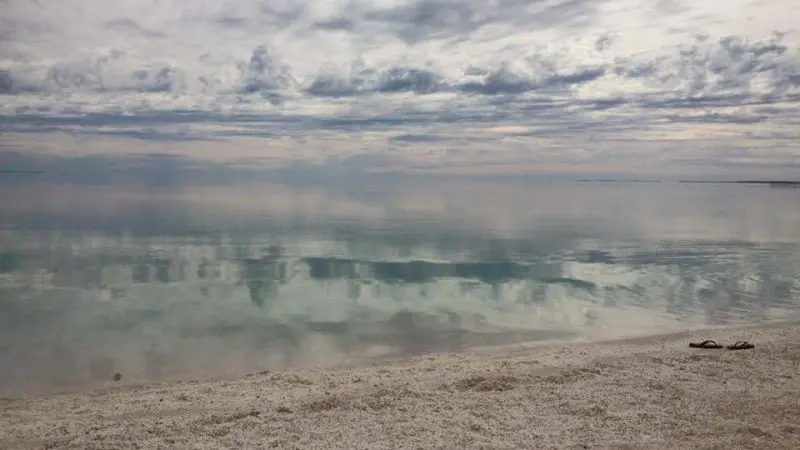 Serene cloudy sky mirrored on tranquil waters at a pristine sandy beach, sandals suggesting an epic 8-Day Perth to Exmouth tour.