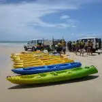 Vibrant kayaks lined up on Rainbow Beach for the Dolphin Kayaking Great Beach Drive Adventure under clear blue Queensland skies.