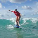 Experience the thrill as a woman in a red shirt surfs Australia’s longest wave on a blue board—perfect for surf lessons and beach drives.