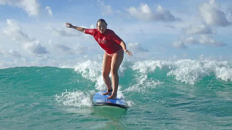 Experience the thrill as a woman in a red shirt surfs Australia’s longest wave on a blue board—perfect for surf lessons and beach drives.