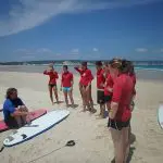 Surf instructor guides red-shirted students mastering surfing techniques on Australia’s renowned longest wave beach for beginners.