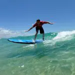 Surfer riding Australia’s longest wave on a blue surfboard, after a picturesque Beach Drive, beneath a vivid clear blue sky.