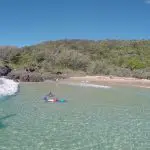 Surfer riding Australia’s longest wave by a scenic island, with another paddler navigating crystal-clear waters nearby.