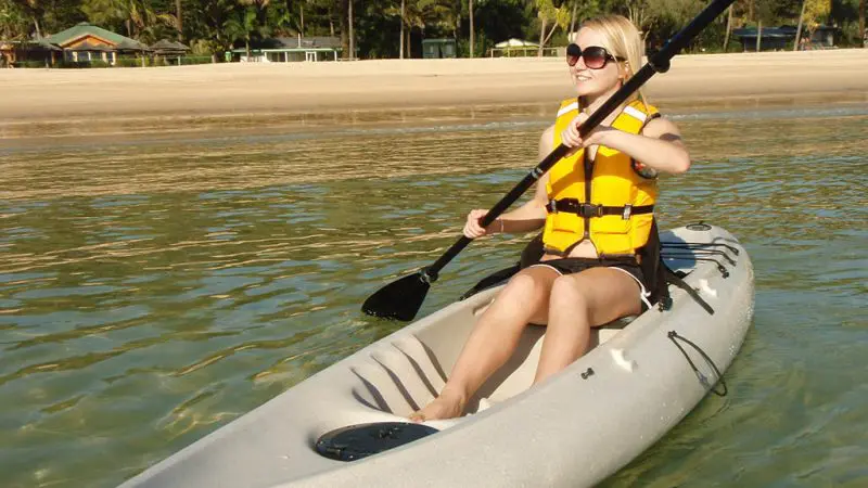 Woman in yellow life jacket kayaking crystal-clear waters by palm-lined Moreton Island beach—iconic Wrecks Adventure Tour experience.