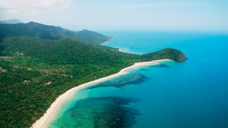 Stunning aerial view of Cape Tribulation on a Daintree Wilderness Tour, featuring lush rainforest, turquoise sea, and pristine white beaches.