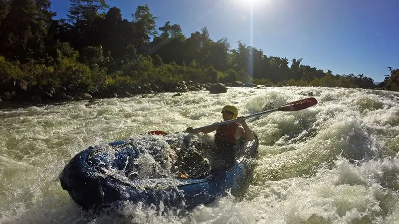 Adventurer kayaking in a blue kayak, navigating intense white-water rapids on a Half Day Sports Rafting tour under sunny, clear skies.