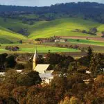Scenic Barossa Valley village with church spire nestled among lush trees and rolling hills, seen on Hop On Hop Off wine tours.