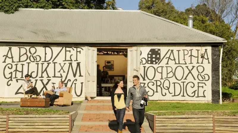 Couple strolling by a winery as groups unwind outdoors during McLaren Vale North Hop On Hop Off Tour, enjoying local experiences.